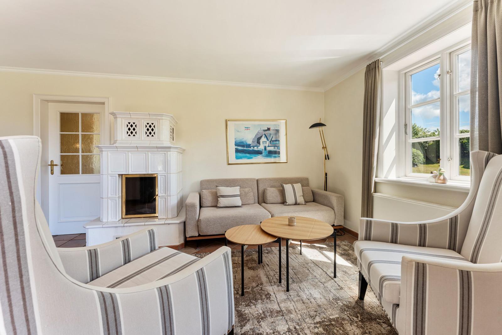 Wohnzimmer mit Sofa, zwei Sesseln, Kamin und Fenster mit Blick nach draußen.