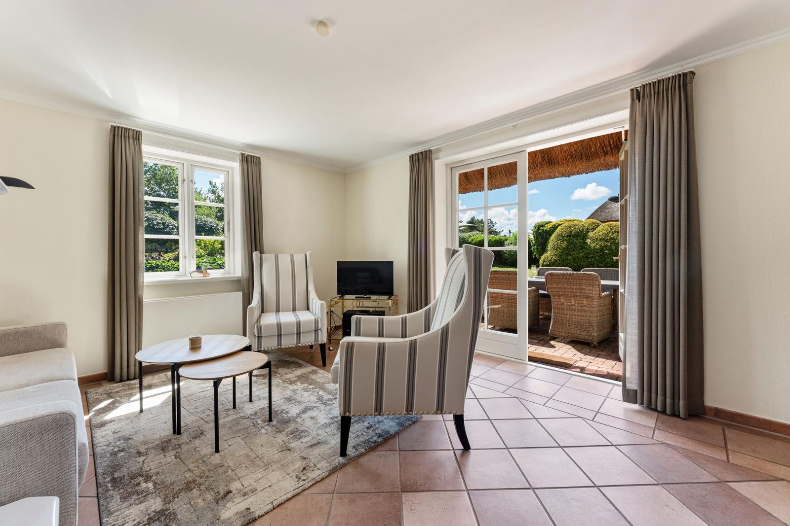 Wohnzimmer mit Sitzgruppe, TV und Blick auf Terrasse mit Garten.