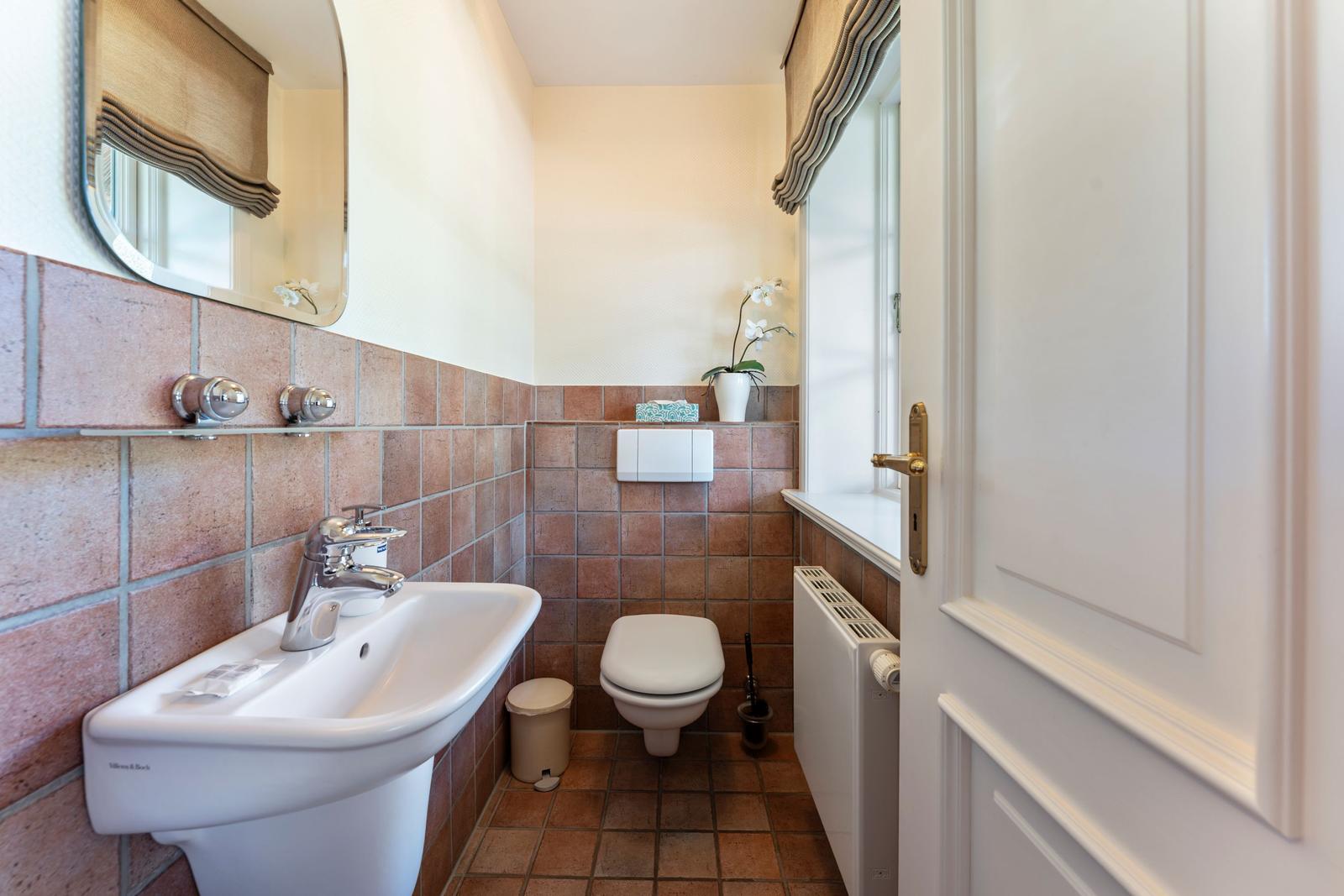 Badezimmer mit Waschbecken, Toilette und Fenster. Wand- und Bodenfliesen in Terrakottaton.