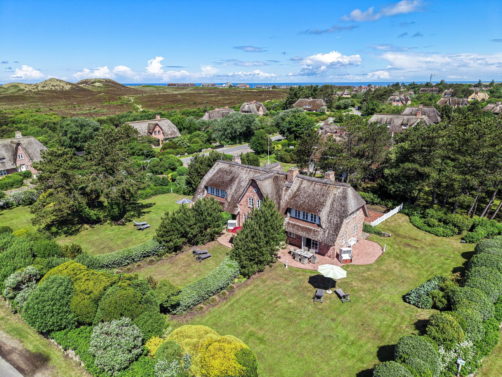 Dorfhaus mit Dachstuhl, umgeben von Grünflächen und Bäumen. Blick auf das Meer.