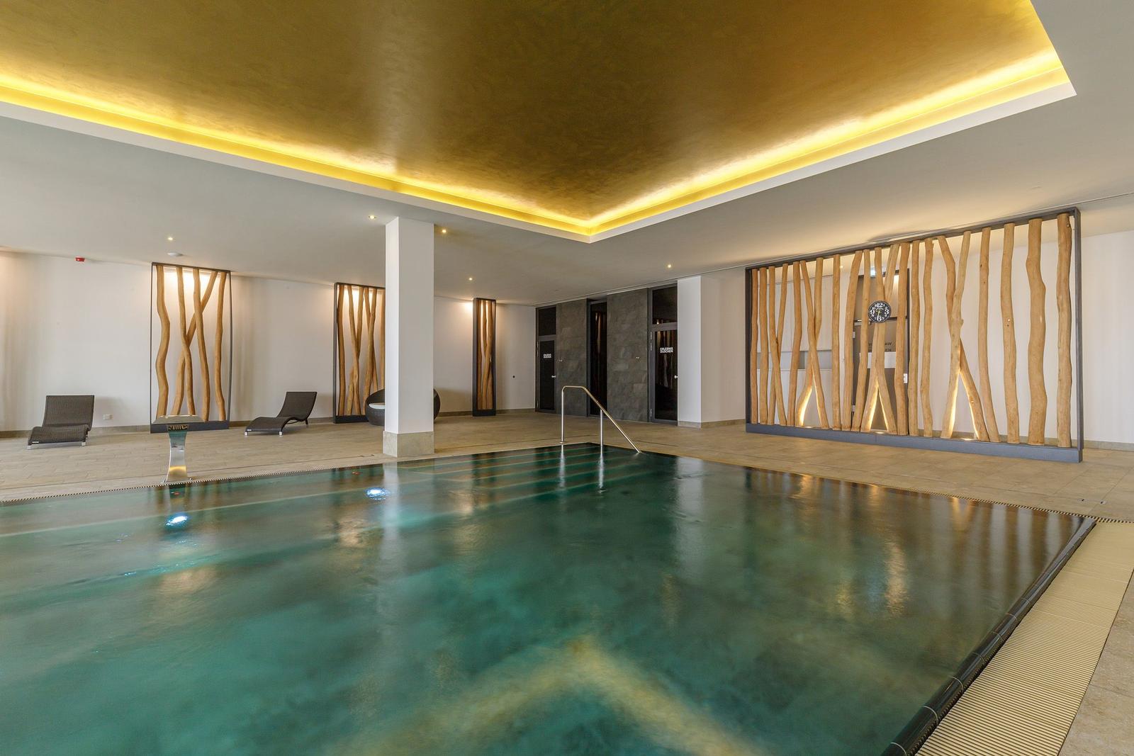 Innenpool mit Holzverkleidung und goldenem Deckenlicht.