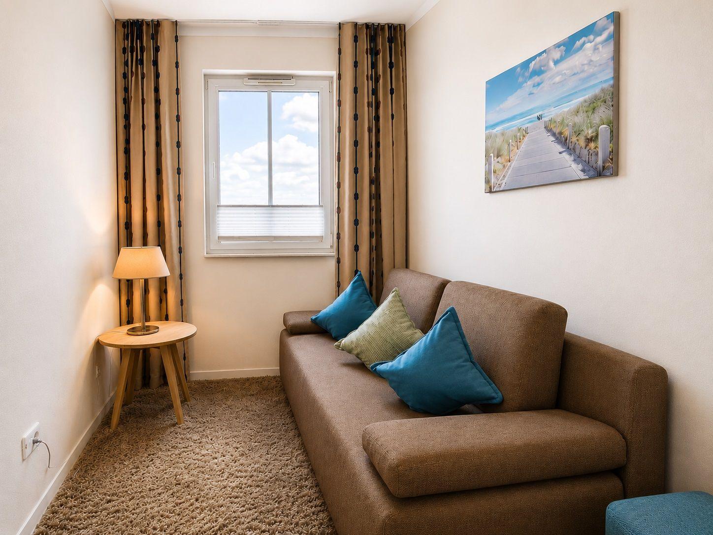 Ein Sofa mit Kissen, Fenster mit Jalousie und Wandbild.