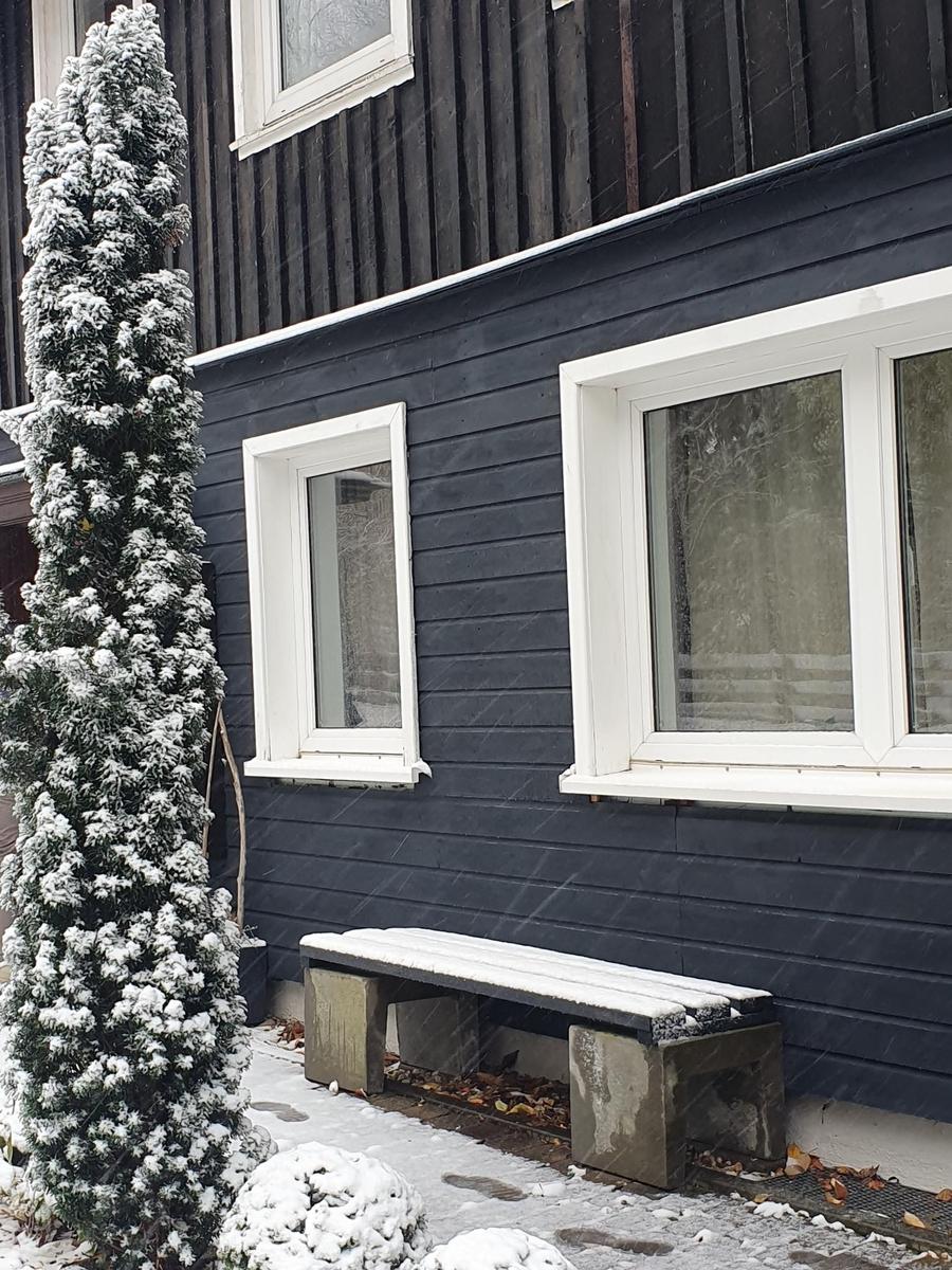 Schneebedeckter Holzausbau mit Fenstern und Bank im Vordergrund.