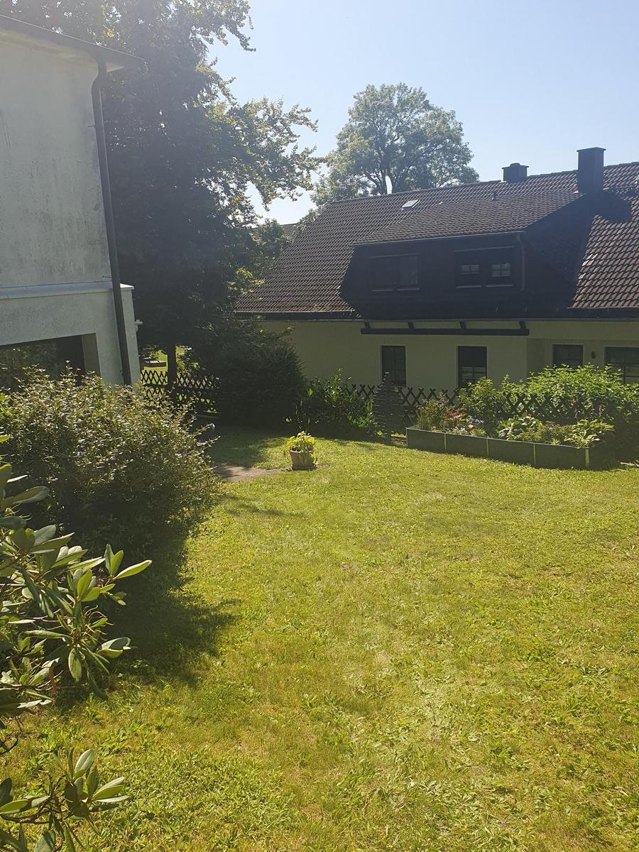 Grüner Garten mit Rasenfläche und Beeten vor einem Haus mit dunklem Dach.