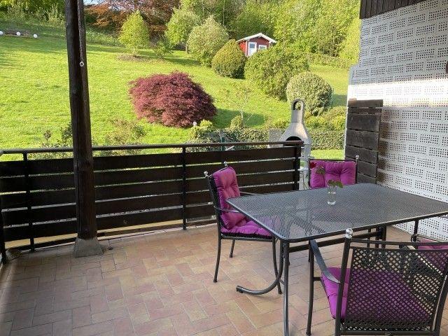 Terrasse mit Tisch, Stühlen und Grill. Blick auf grünen Garten und Wald.