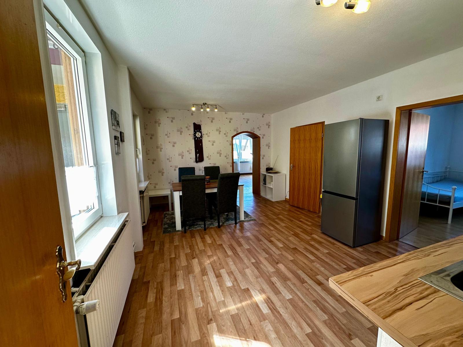 Wohnung mit Essbereich, Küchenzeile und Schlafzimmer. Holzboden und Kühlschrank sichtbar.