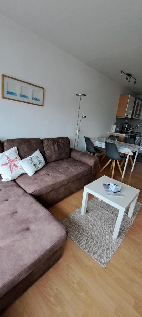 Wohnzimmer mit Sofa, Esstisch und Küchenbereich. Holzboden und Wandbild mit Meeresmotiven.