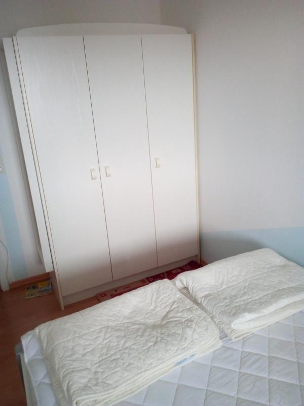 Schlafzimmer mit Bett und weißen Kleidern. Hinter dem Bett steht ein großer Schrank.
