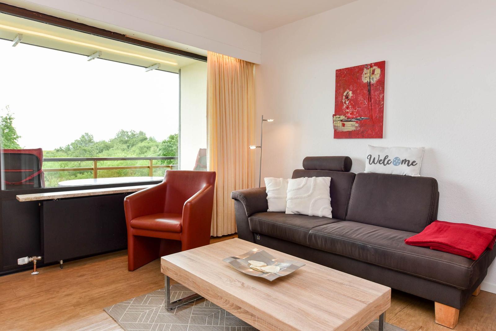 Wohnzimmer mit Sofa, Sitzgelegenheit und Blick auf Balkon mit Grün.
