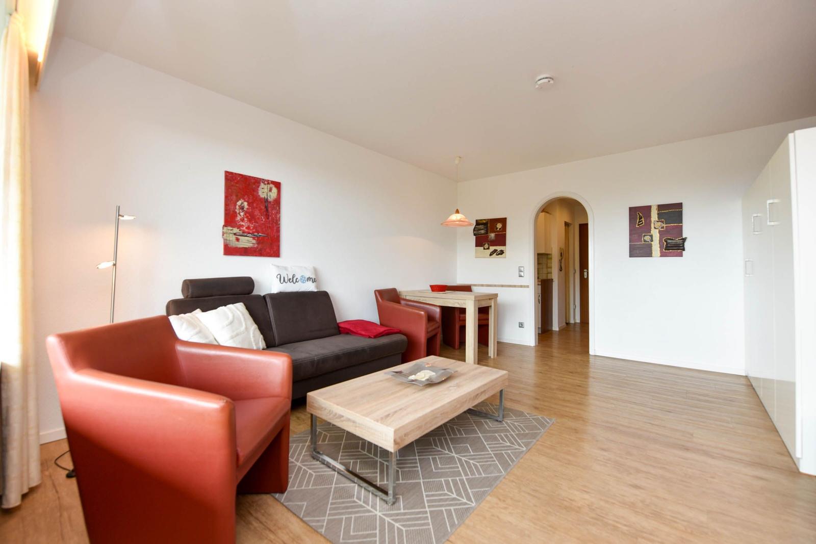 Wohnbereich mit Sofa, Sessel und Esstisch. Holzboden und Wandbilder.
