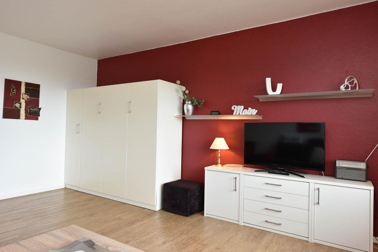 Zimmer mit roter Wand, weißem Schrank und Fernseher auf Kommode.