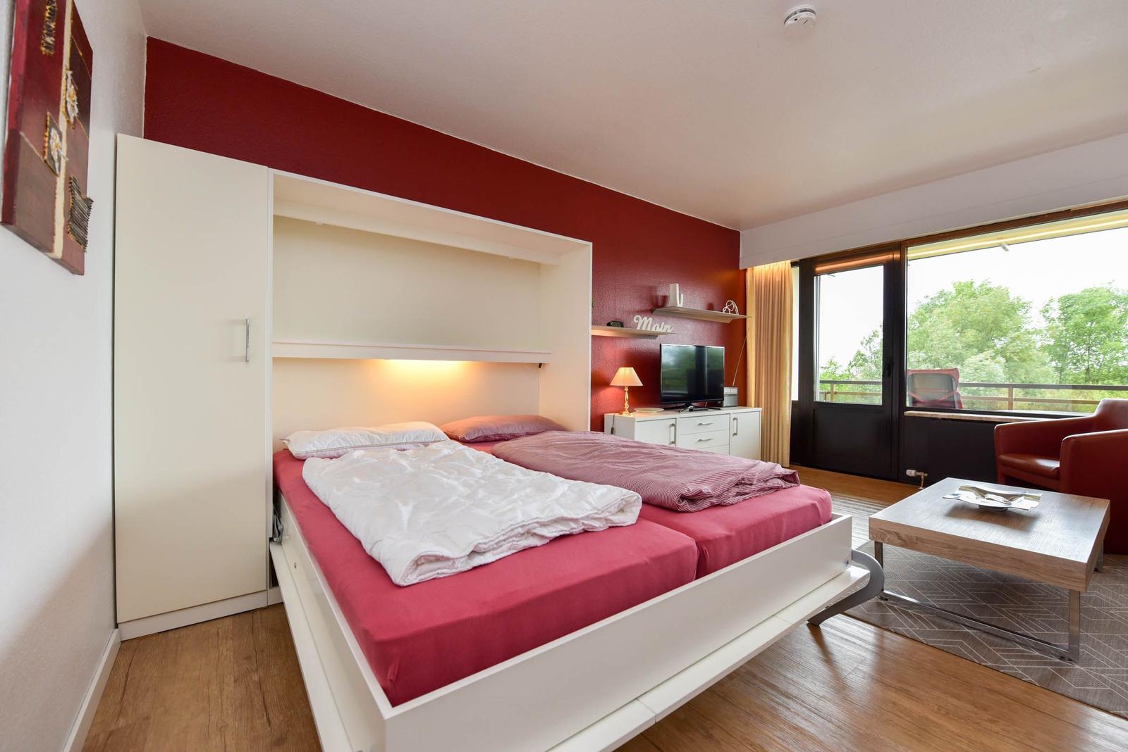 Schlafzimmer mit Bett, Fernseher und Balkonansicht.