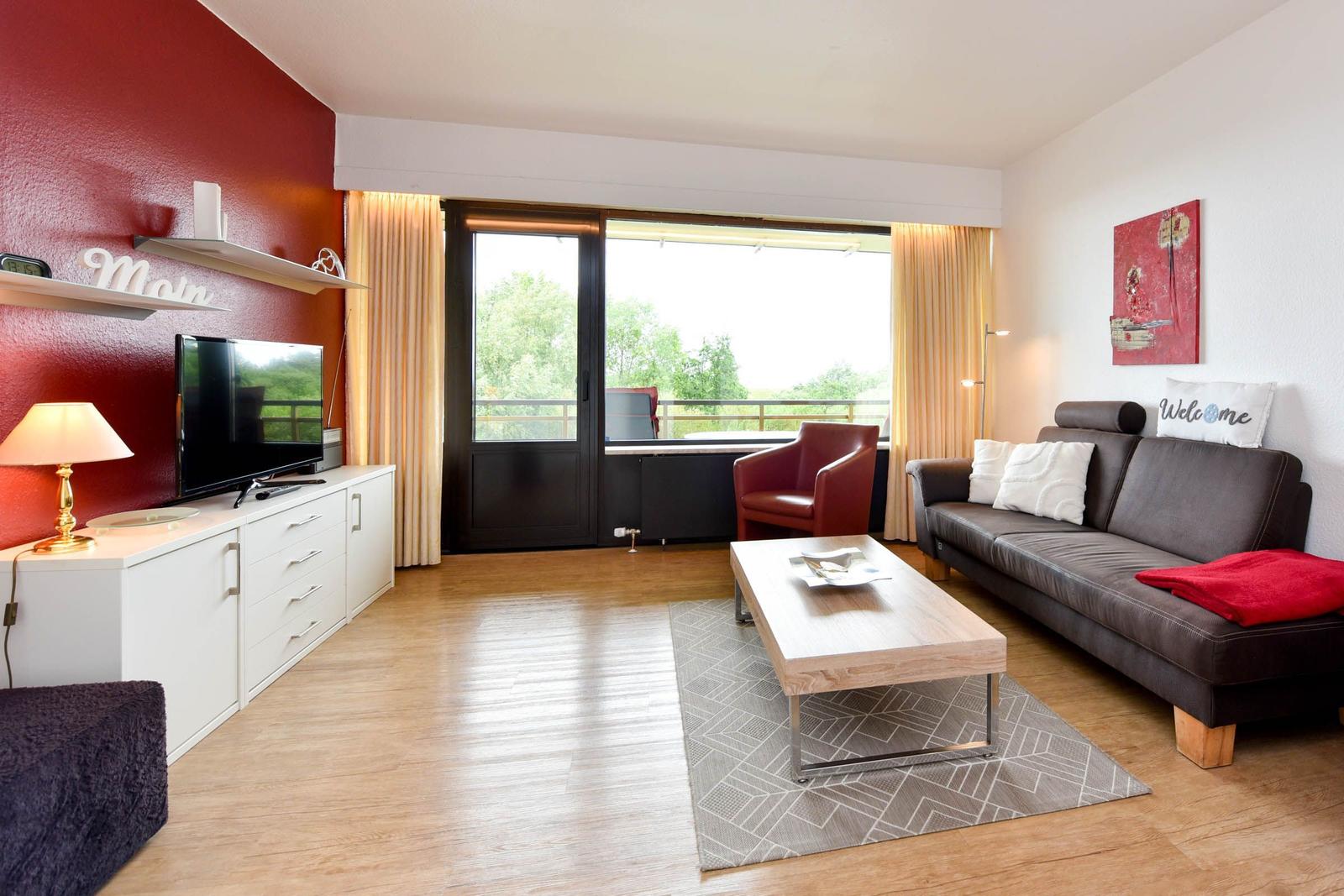 Wohnzimmer mit Sofa, Couchtisch und TV. Balkon mit Blick auf Grünflächen.