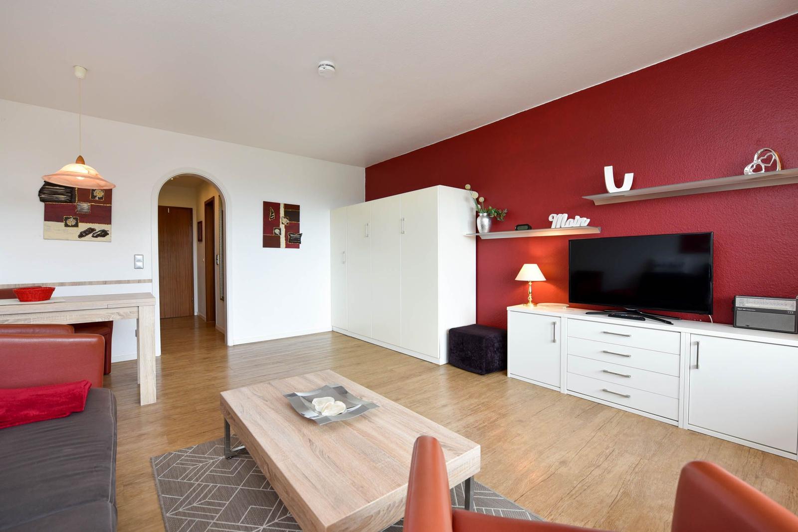 Wohnzimmer mit roter Wand, TV, Schrank und Holzboden.