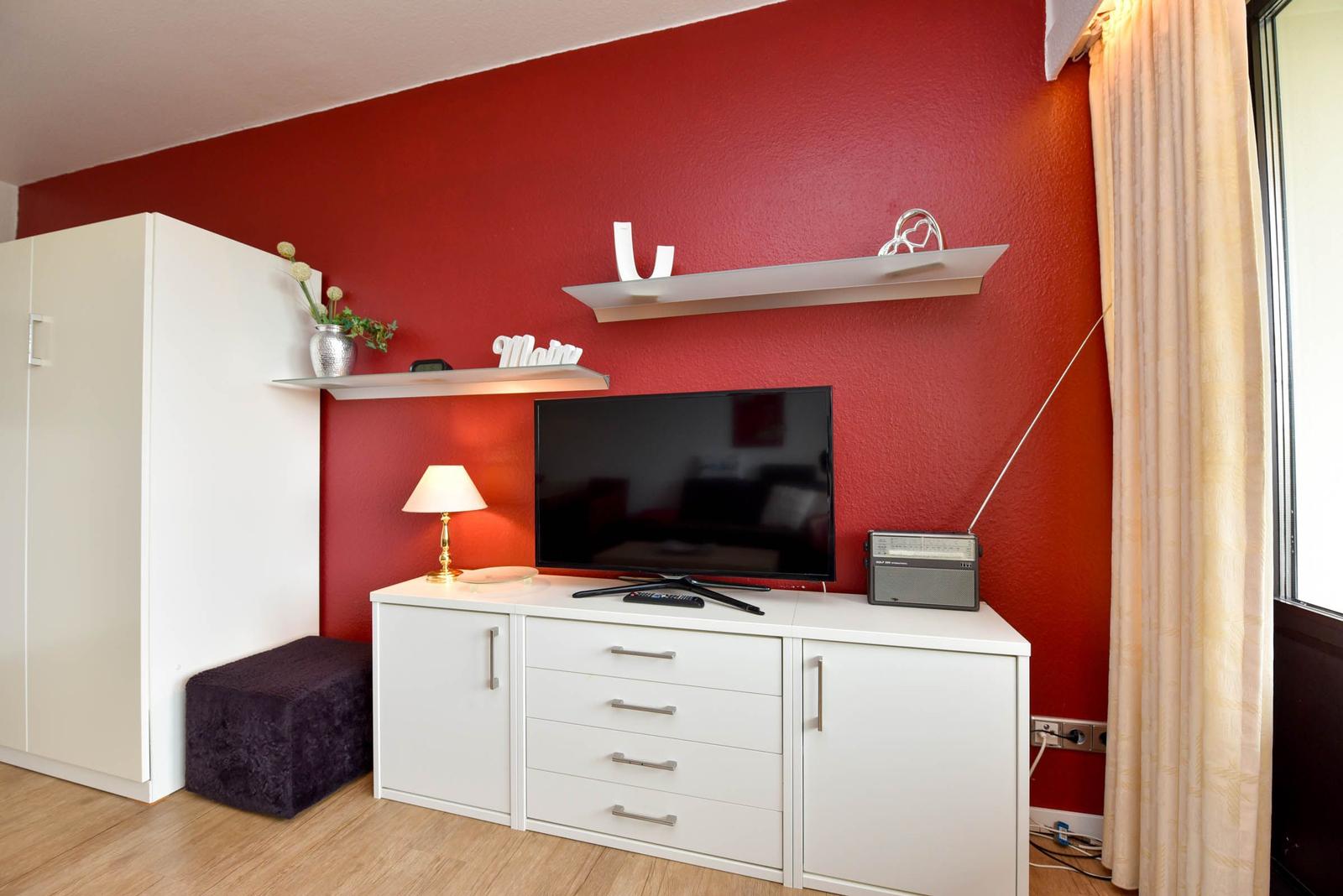 Rotes Wand mit TV-Schrank, Lampe, Regal und Schrank.