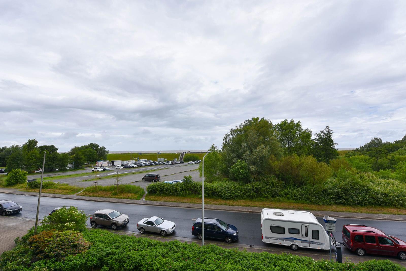 Aussicht auf Parkplatz mit Autos und Wohnwagen, umgeben von Grünflächen und Bäumen unter bewölktem Himmel.