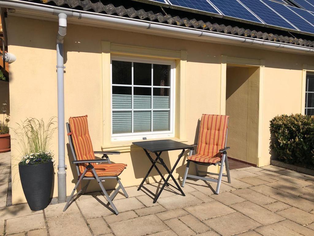 Terrace with two orange chairs and a table. Background: house wall and window.