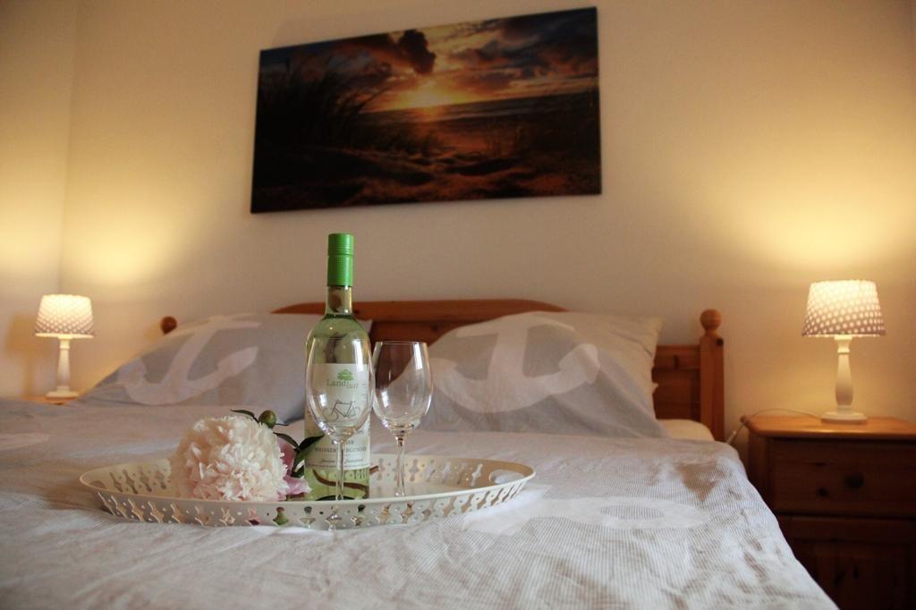 A bed with pillows, a bottle of wine, and two glasses on a tray.