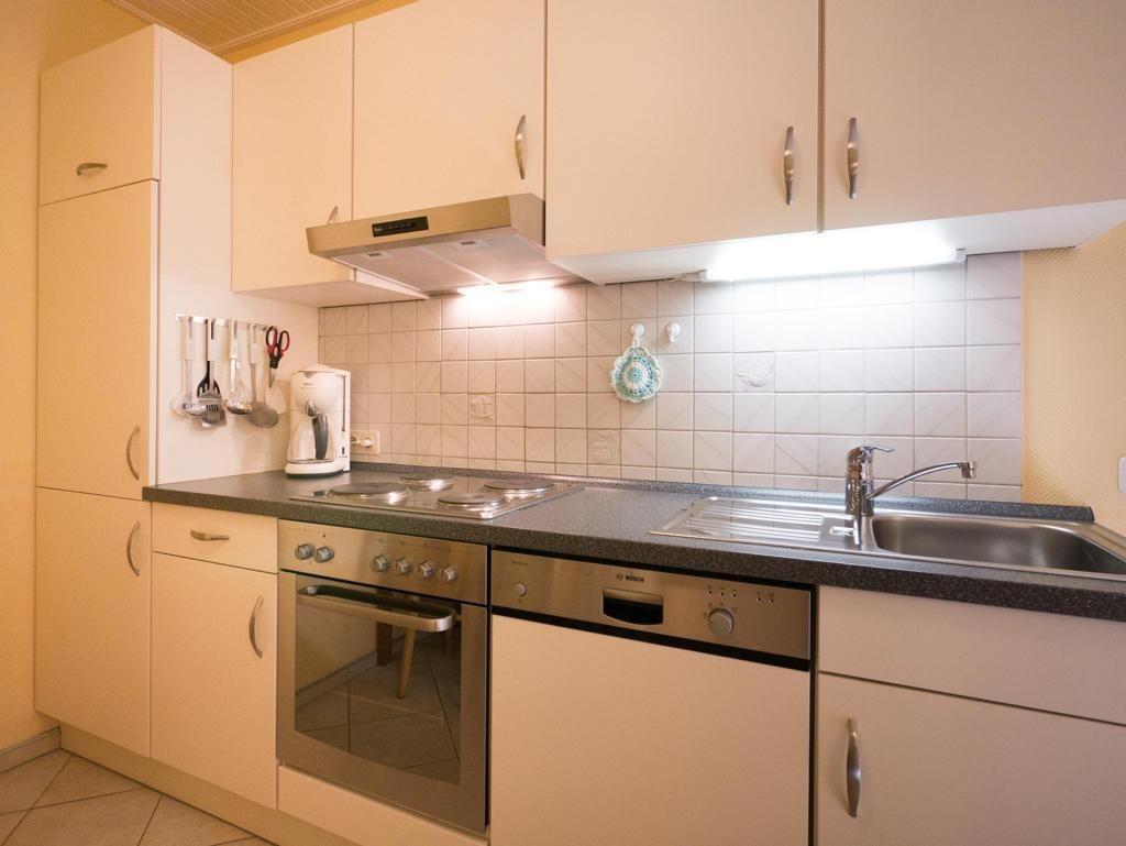 Kitchen with worktop, sink, stove, oven, cabinets, and wall tiles.