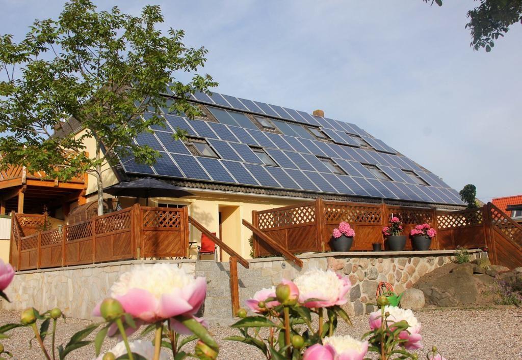 House with solar panels, wooden railings, and flower beds in the garden.