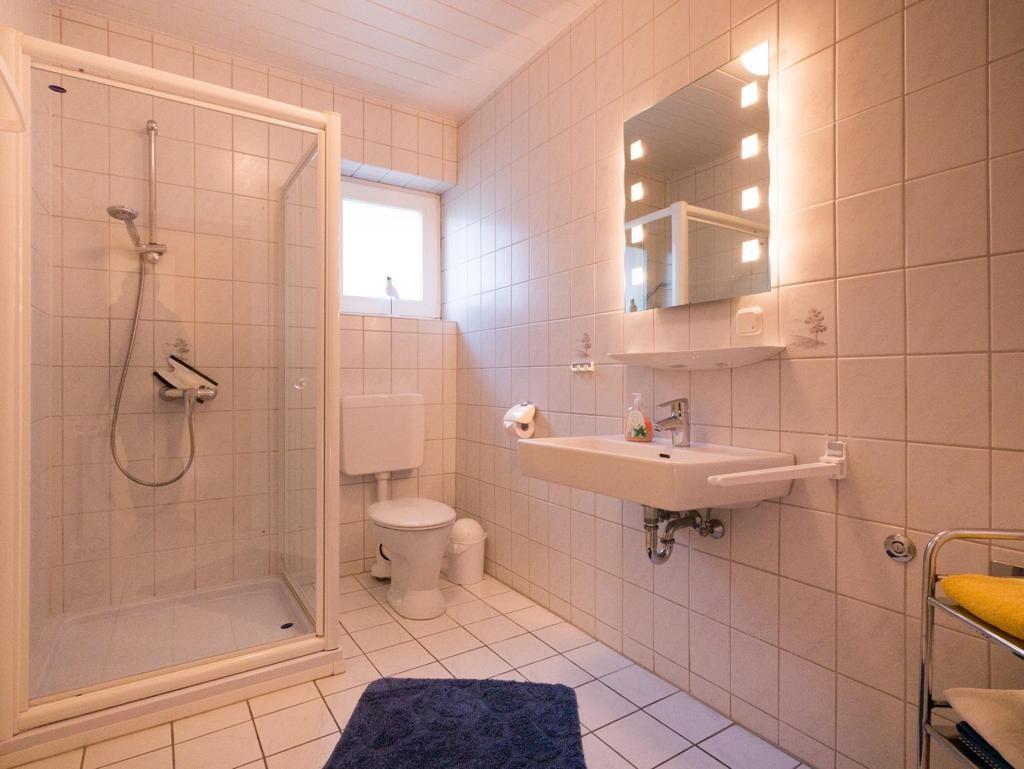 Bathroom with shower, toilet, and sink with lit mirror.