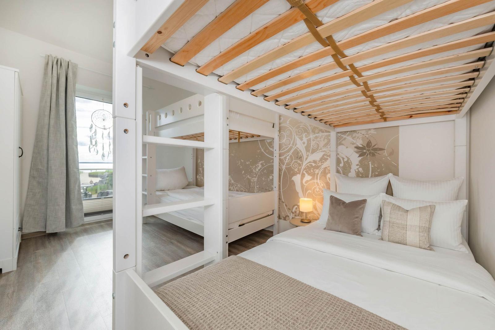 Schlafzimmer mit Doppelbett und Doppelstockbetten, Holzdecke und Fenster mit Vorhang.