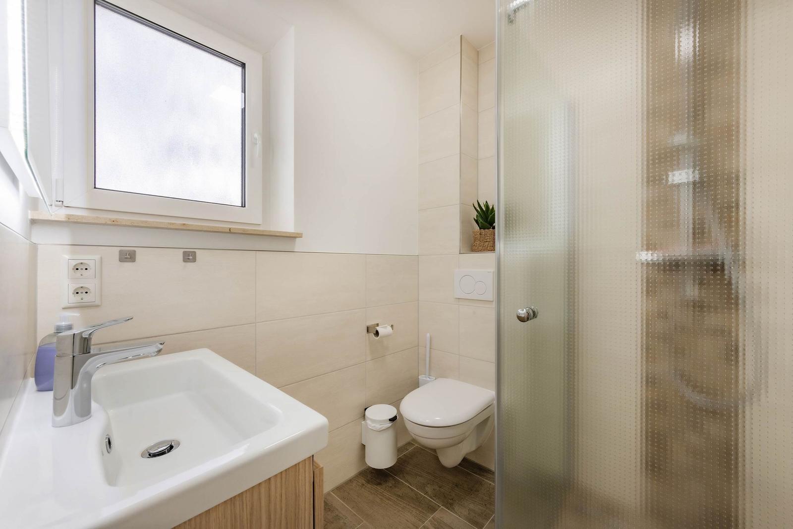 Badezimmer mit Dusche, Toilette und Waschbecken unter Fenster