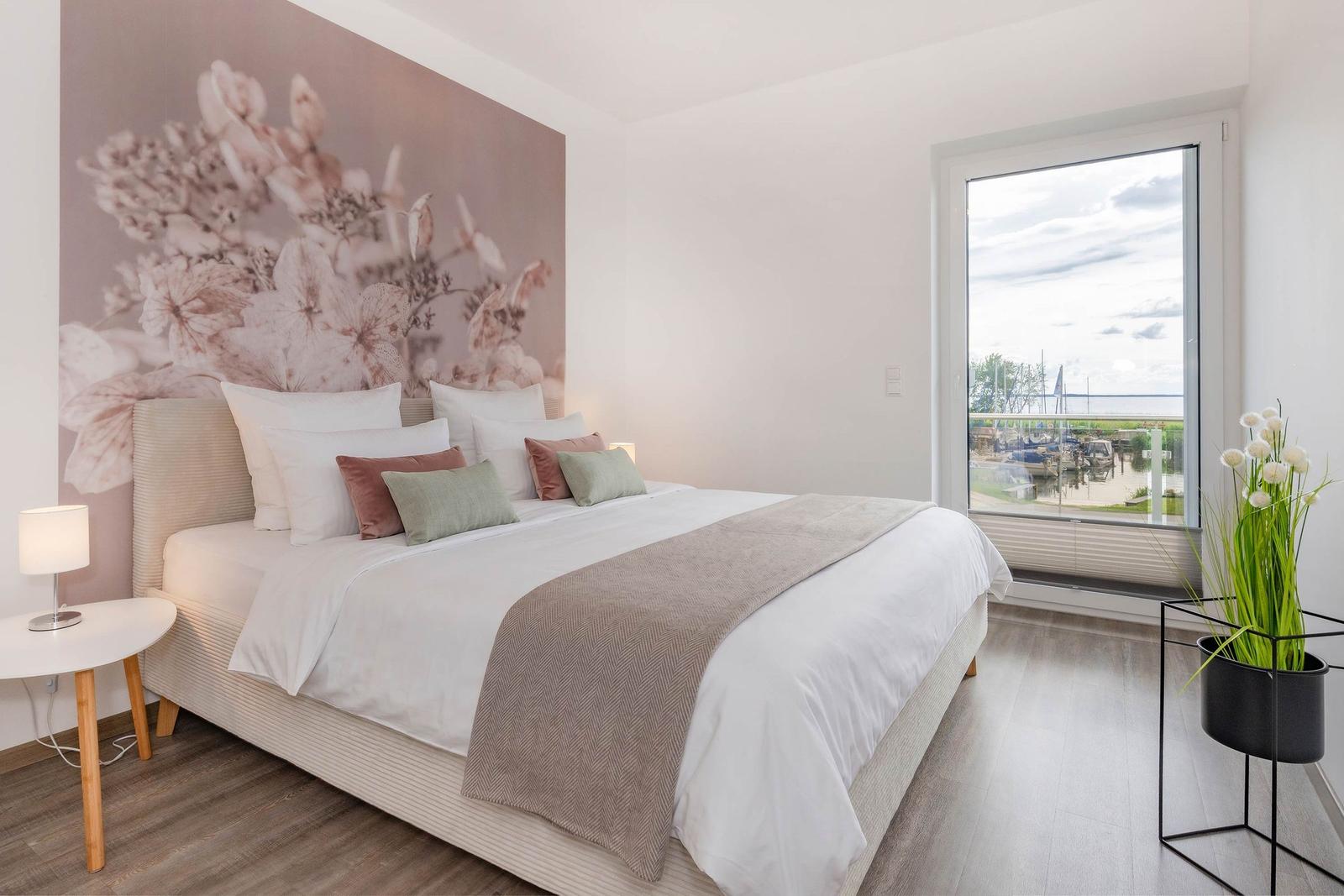 Schlafzimmer mit Bett, Wandbild und Blick auf den Hafen.