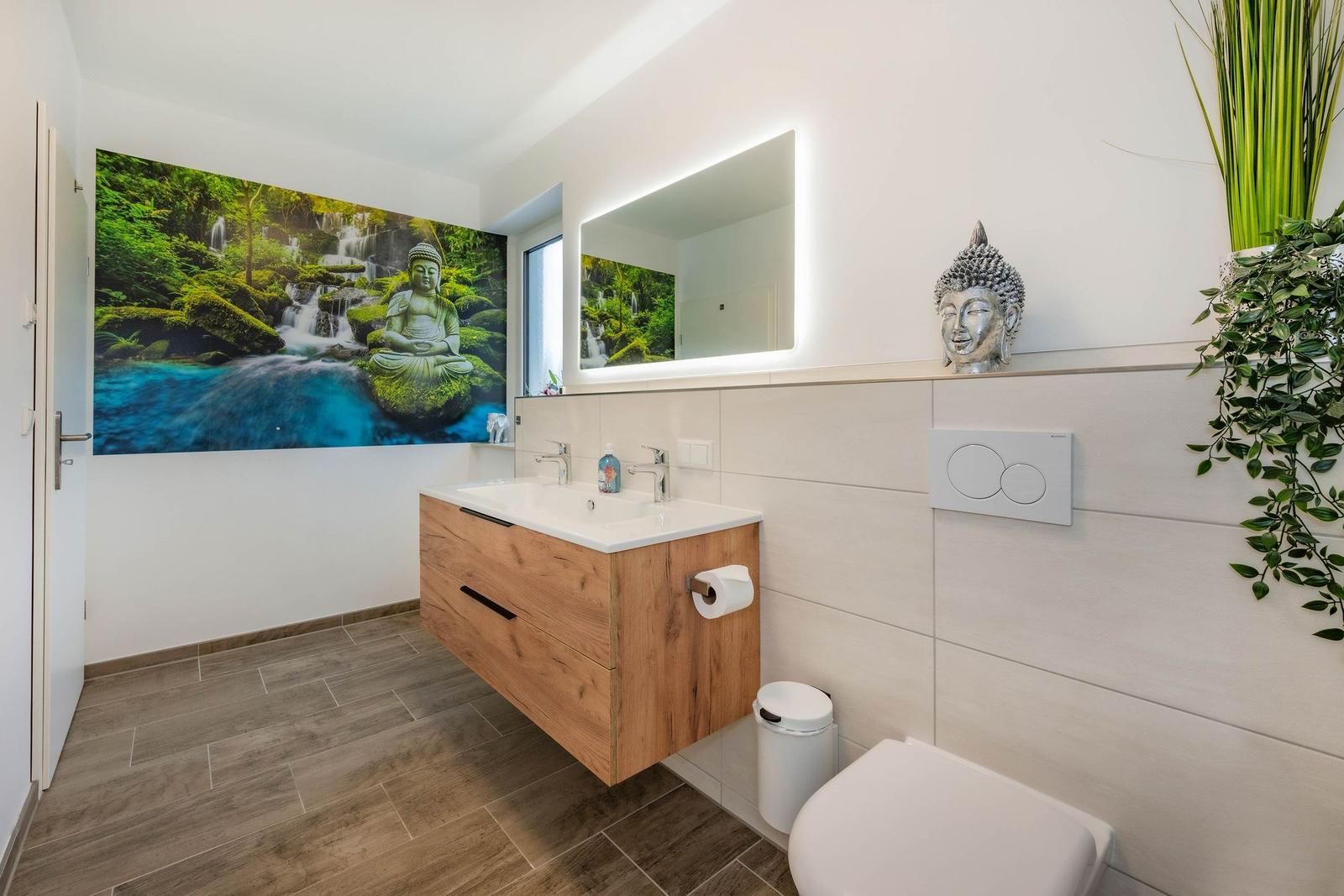 Badezimmer mit Holzwaschtisch, Spiegel und Buddha-Dekoration an der Wand.
