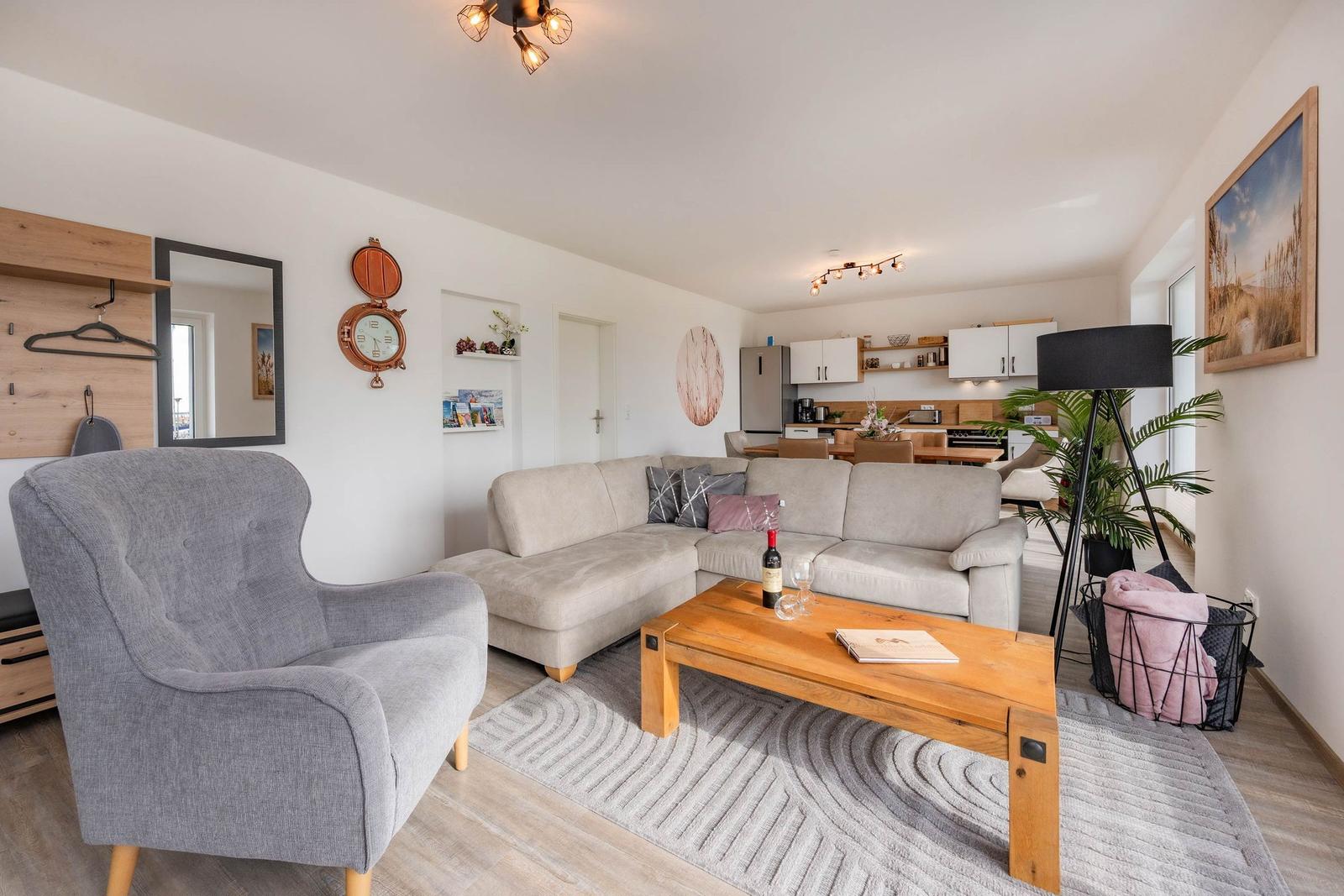 Wohnzimmer mit Sofa, Sessel und Holztisch. Küche im Hintergrund.