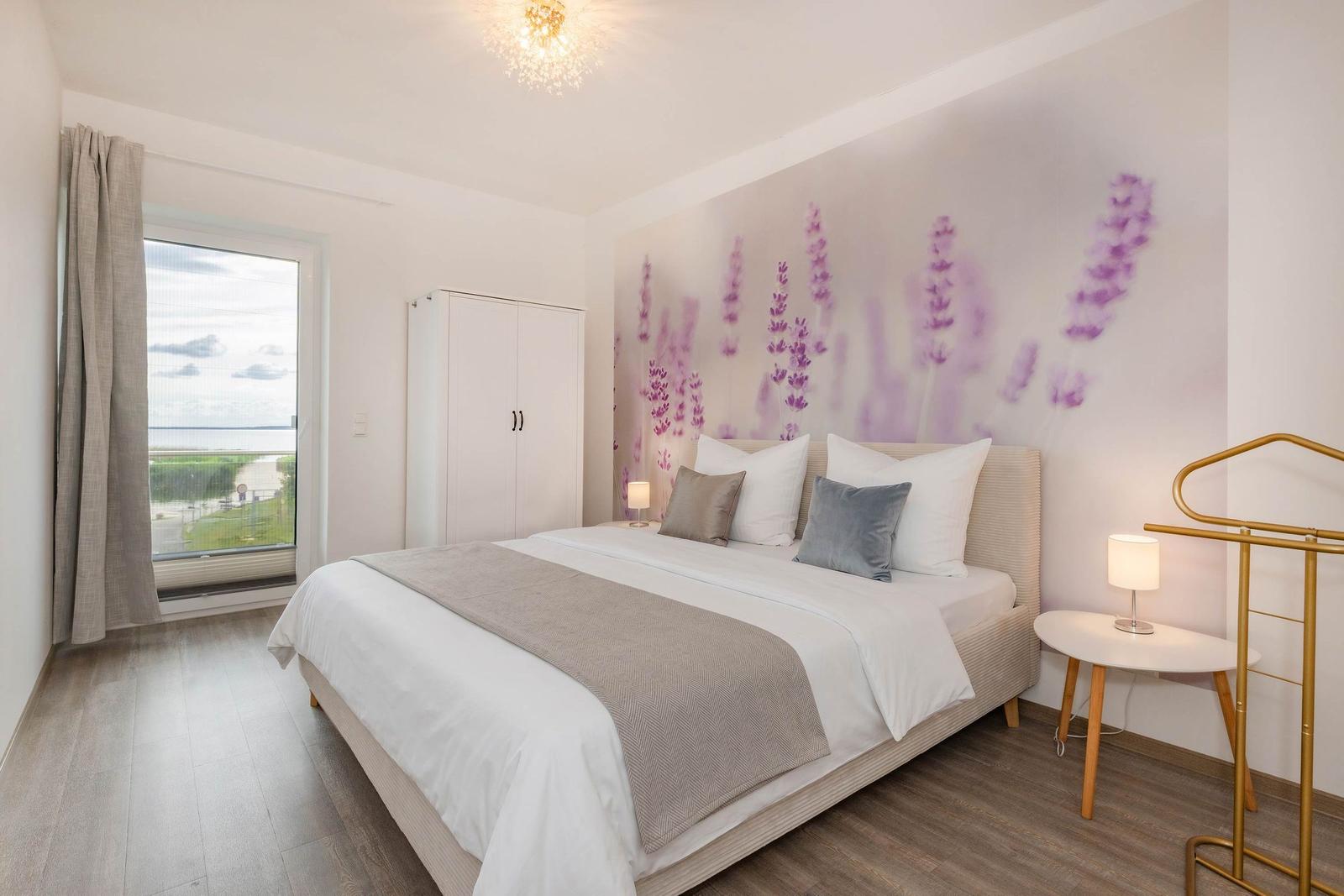 Schlafzimmer mit Bett, Wandtapete und Fensterblick auf Wasser