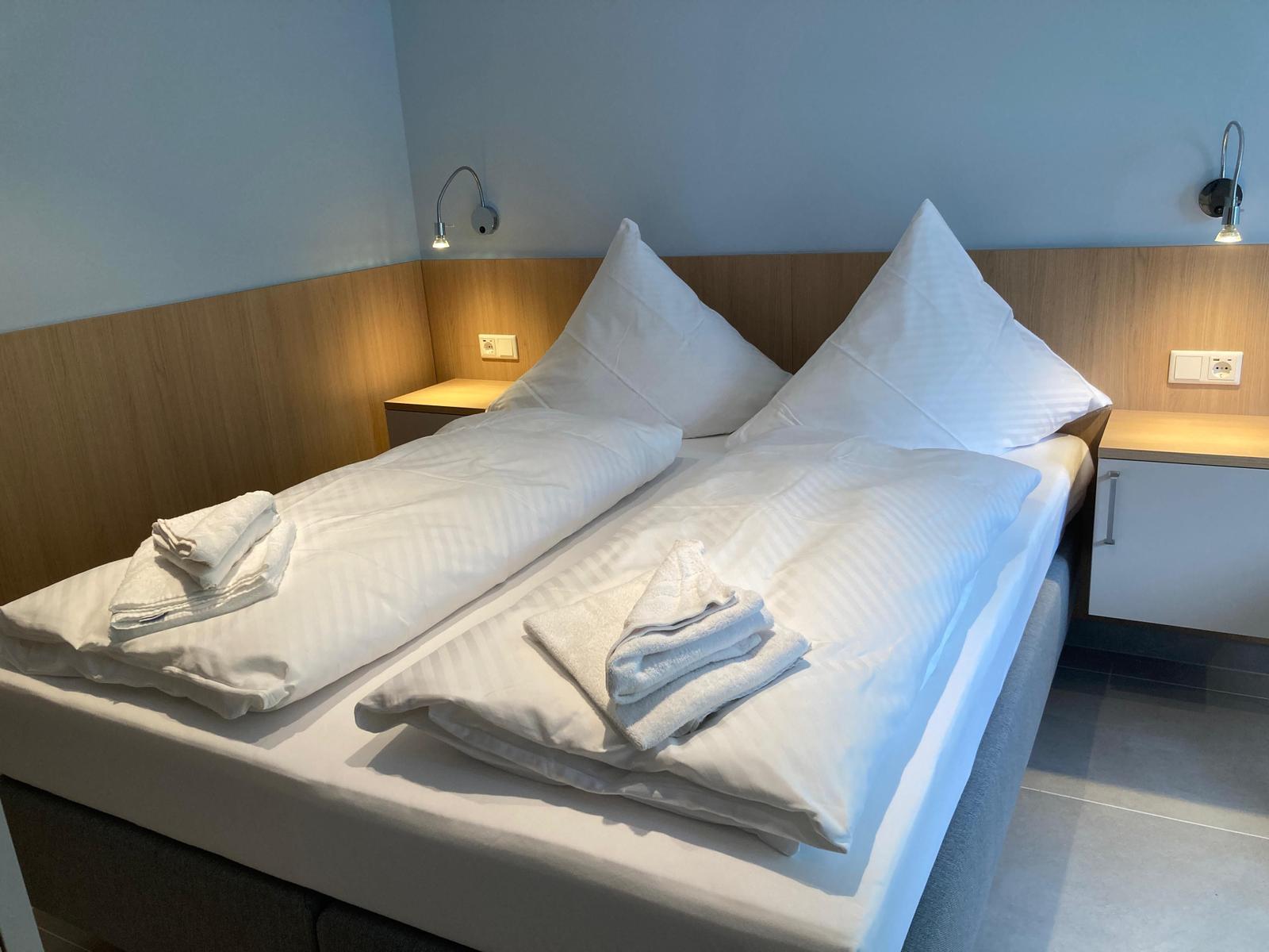 Doppelbett mit weißen Laken und Handtüchern, Holzpaneelen und Wandlampen.