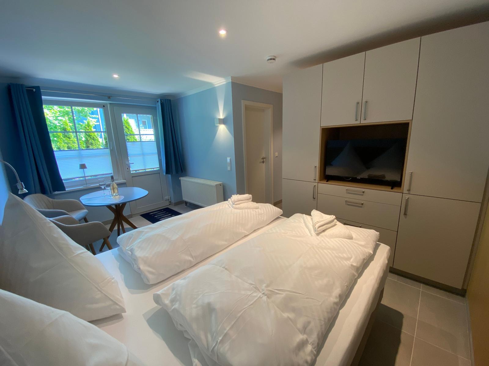 Schlafzimmer mit Doppelbett, TV und Fenster mit Blick auf Grün.