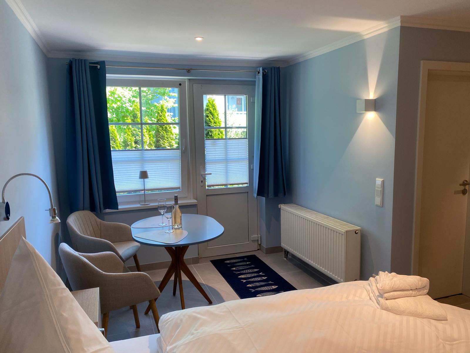 Schlafzimmer mit Bett, Tisch, zwei Stühlen und Fenster mit Blick auf Grün.