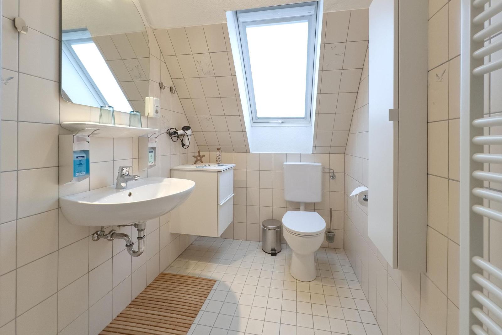 Badezimmer mit Waschbecken, Toilette und Dachfenster. Fliesenwand und Holzmatte.