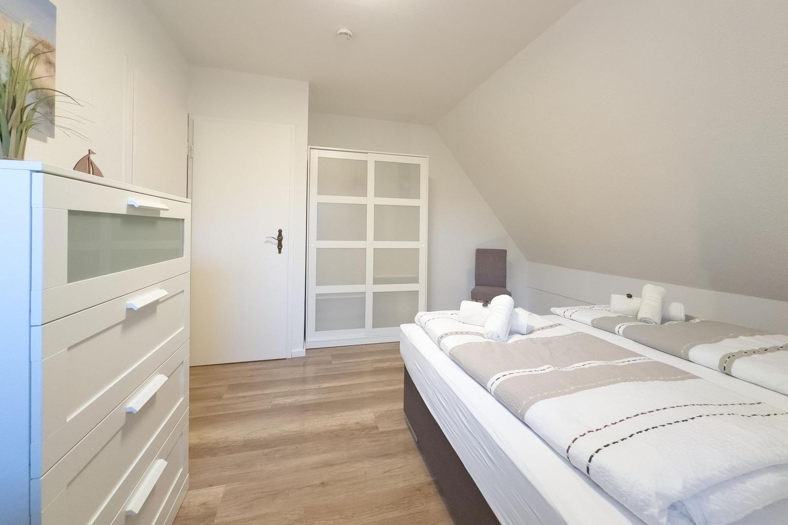 Zimmer mit Doppelbett, Schrank und Holzboden. Dachschräge und Fenster sichtbar.