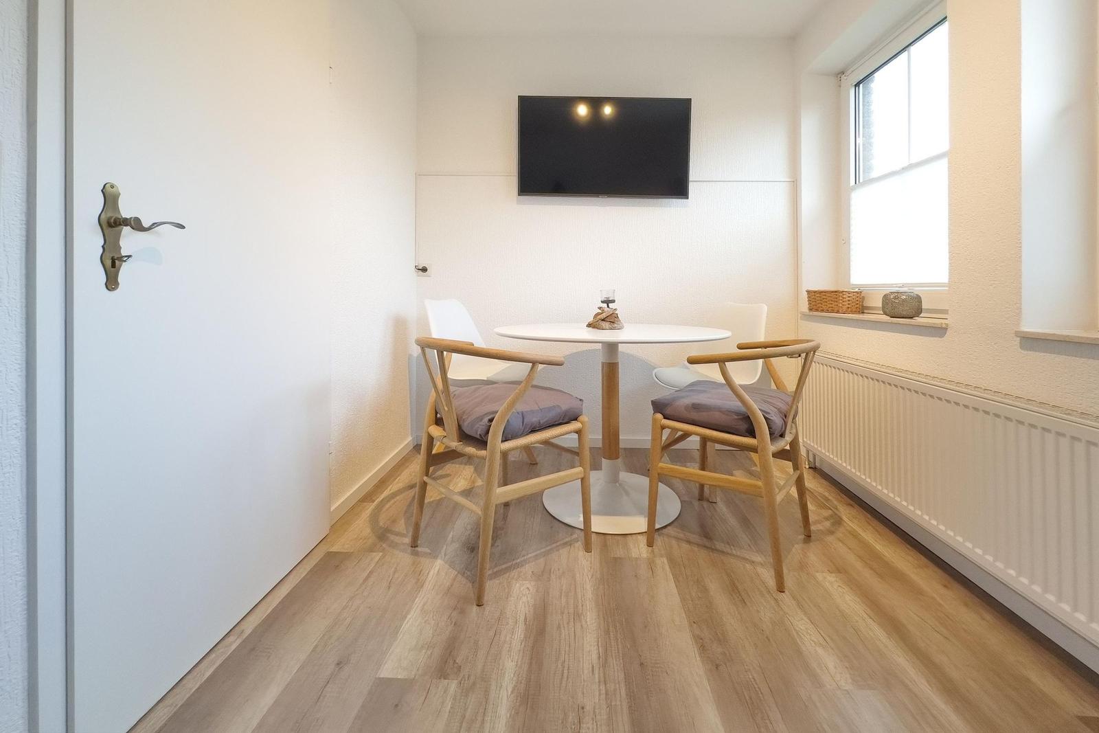 Ein Essbereich mit runden Tisch, zwei Stühlen und Fernseher an der Wand.