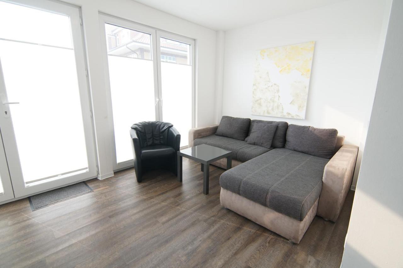 Wohnzimmer mit Sofa, Sessel und Glas-Tisch. Große Fenster und Holzboden.