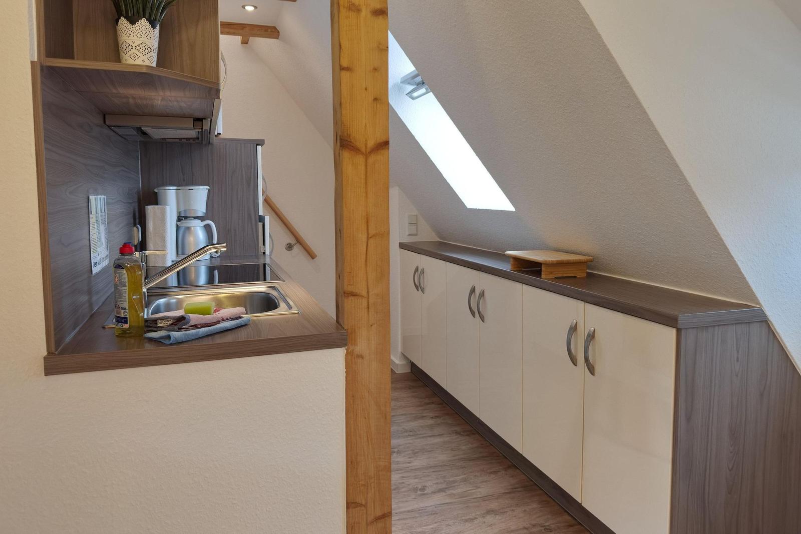 Küche mit Spüle, Kaffeemaschine und Schränken unter Dachschrägen.