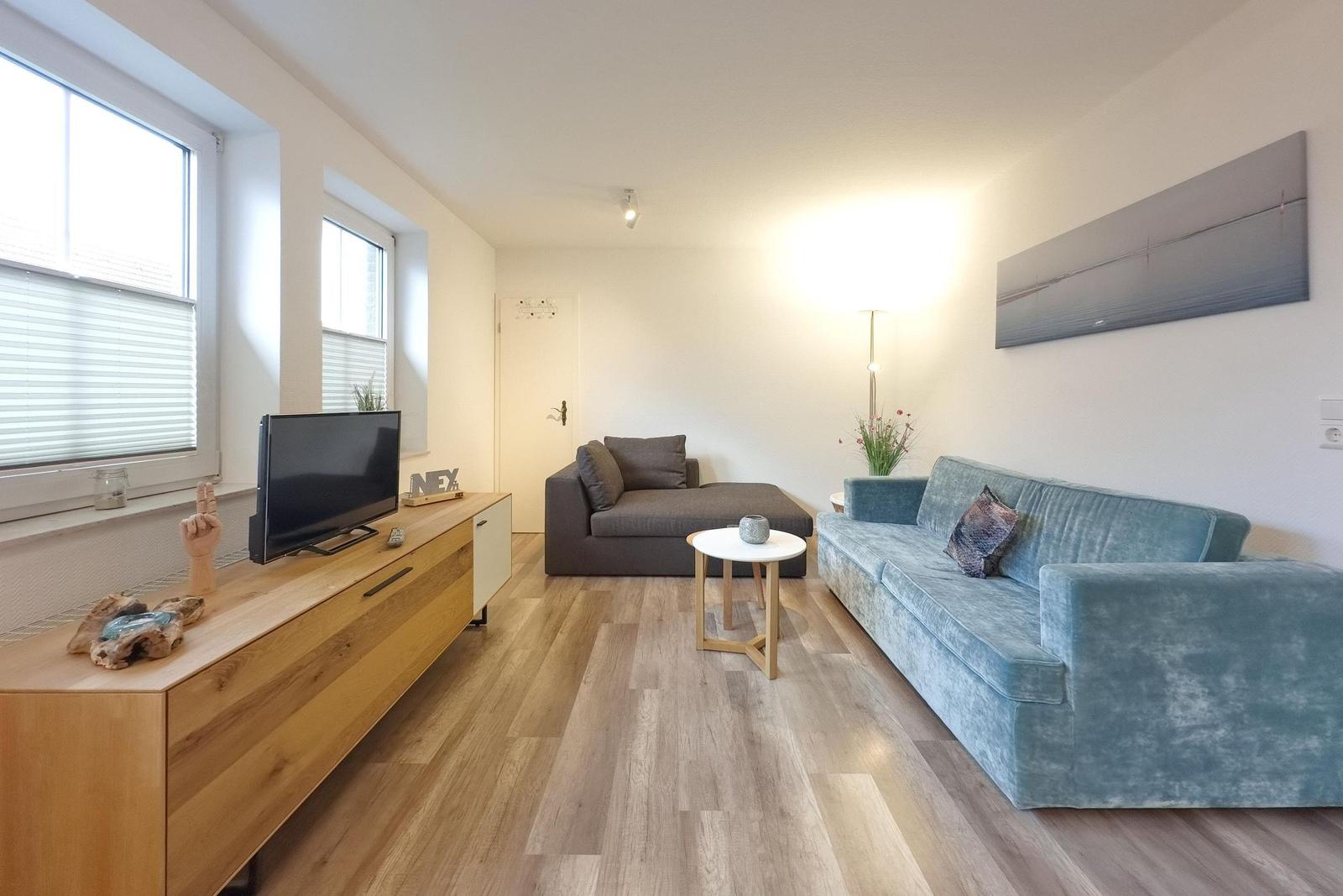 Wohnzimmer mit blauem Sofa, Holzboden und Fernseher auf Schrank
