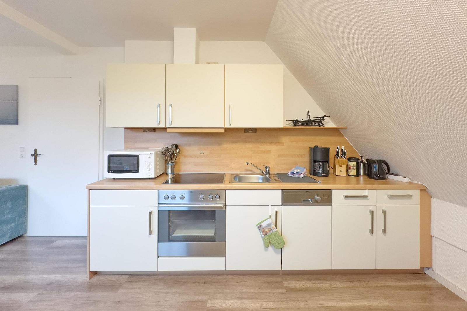 Küche mit weißen Schränken, Holz Arbeitsplatte und Edelstahl Geräten unter schrägem Dach