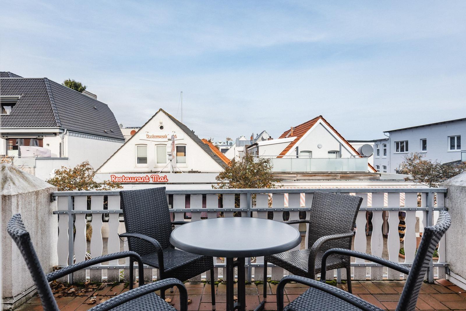Terrasse mit Tisch und Stühlen. Blick auf Gebäude und Restaurant Mai.