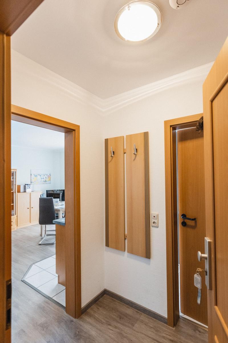 Flur mit Holztüren, Kleiderhaken und Sicht auf Wohn- und Arbeitszimmer.