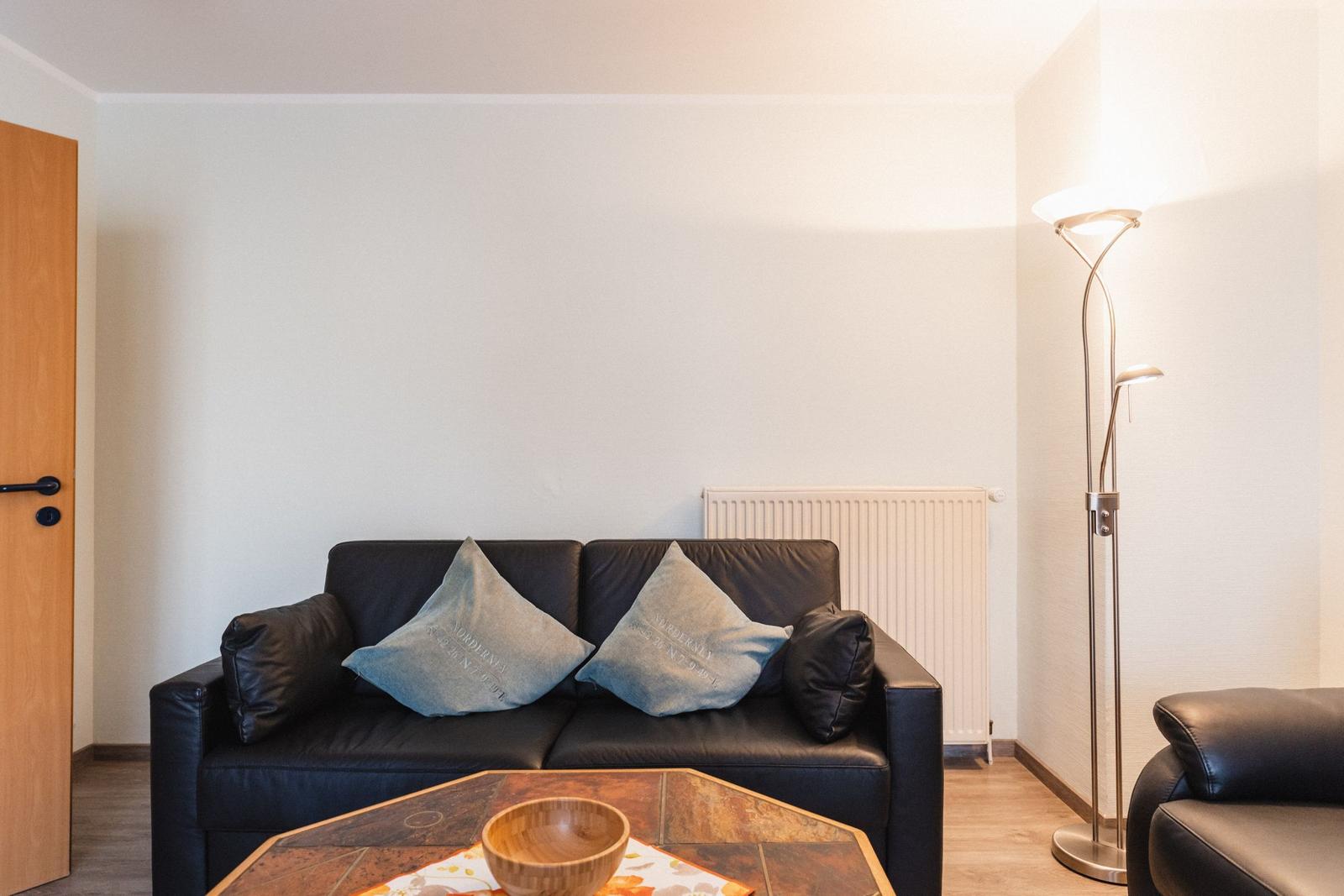 Schwarzes Sofa mit Kissen, Tisch und Stehlampe im Wohnzimmer.