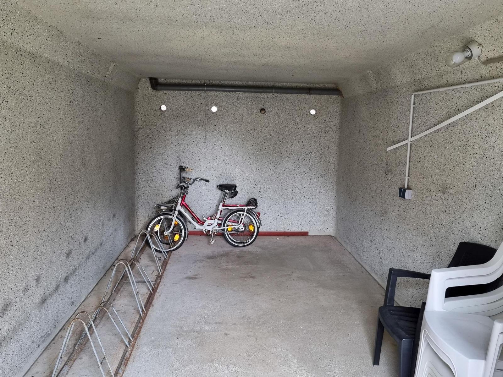 Ein Fahrrad steht in einer Garage mit Stahlregal und Plastikstühlen.
