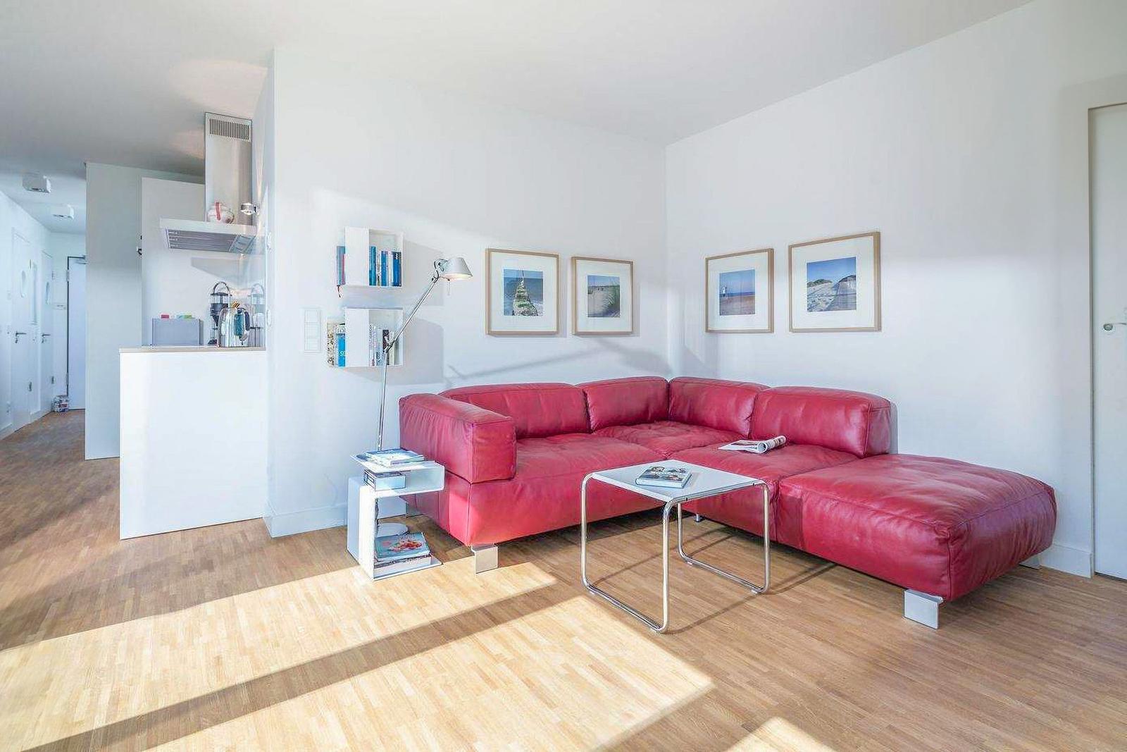 Ein Wohnzimmer mit rotem Sofa, Glas-Tisch und Holzboden. An der Wand hängen Bilder.