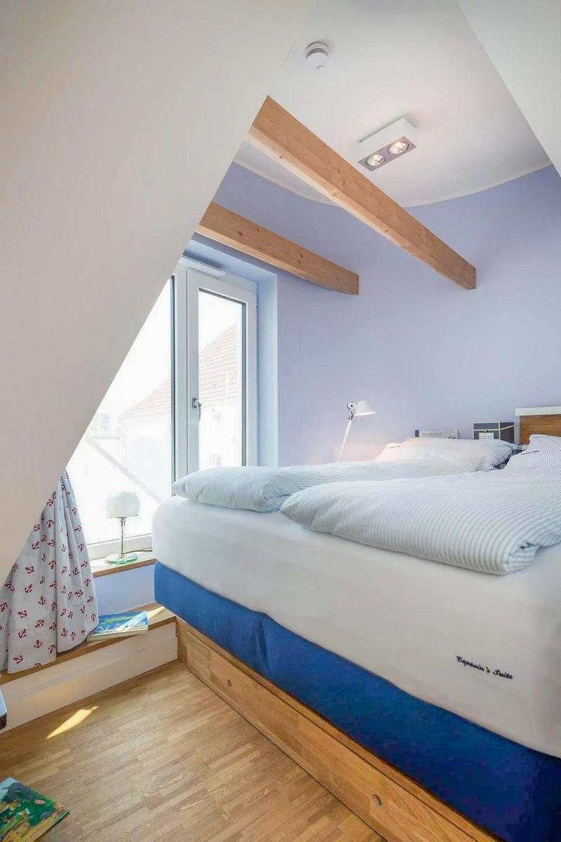 Schlafzimmer mit Dachschrägen, Holzbalken und blau-weißem Bett.