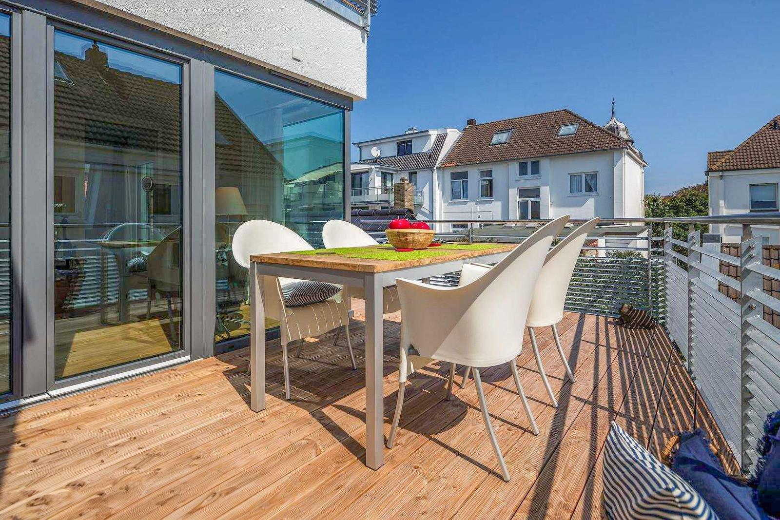 Terrasse mit Tisch und Stühlen, Holzboden, Blick auf Gebäude.
