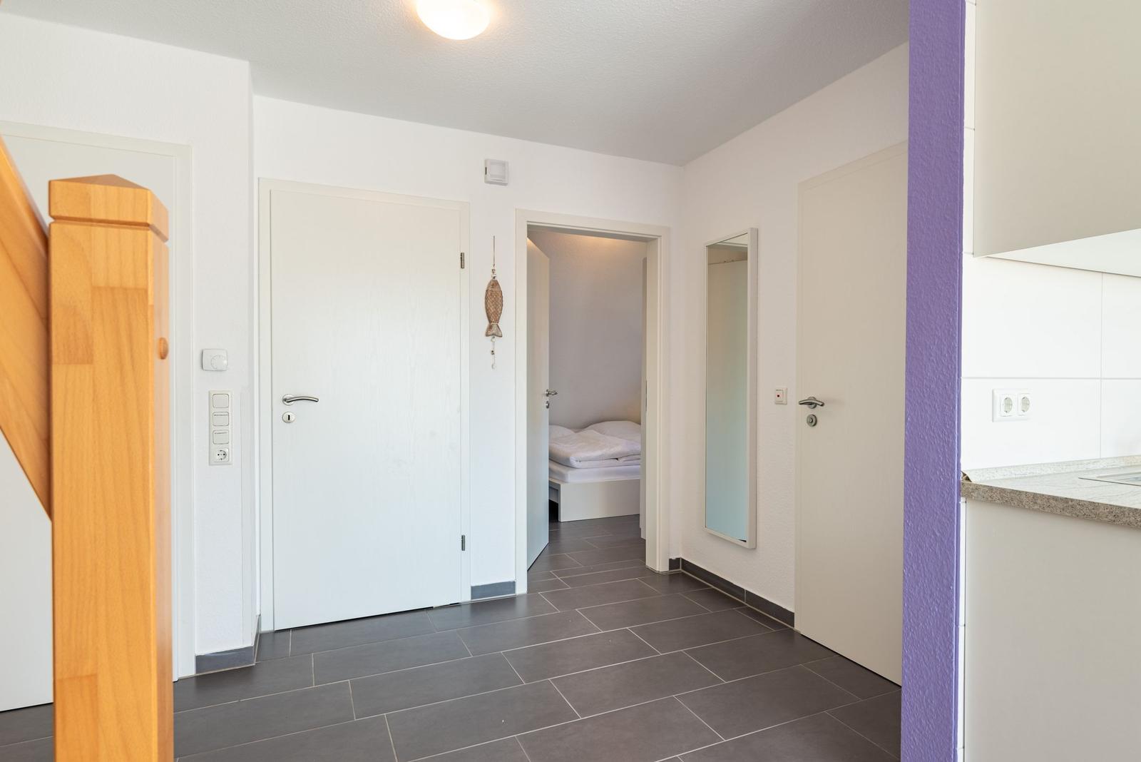 Flur mit Tür, Spiegel und Blick in Schlafzimmer mit Bett.