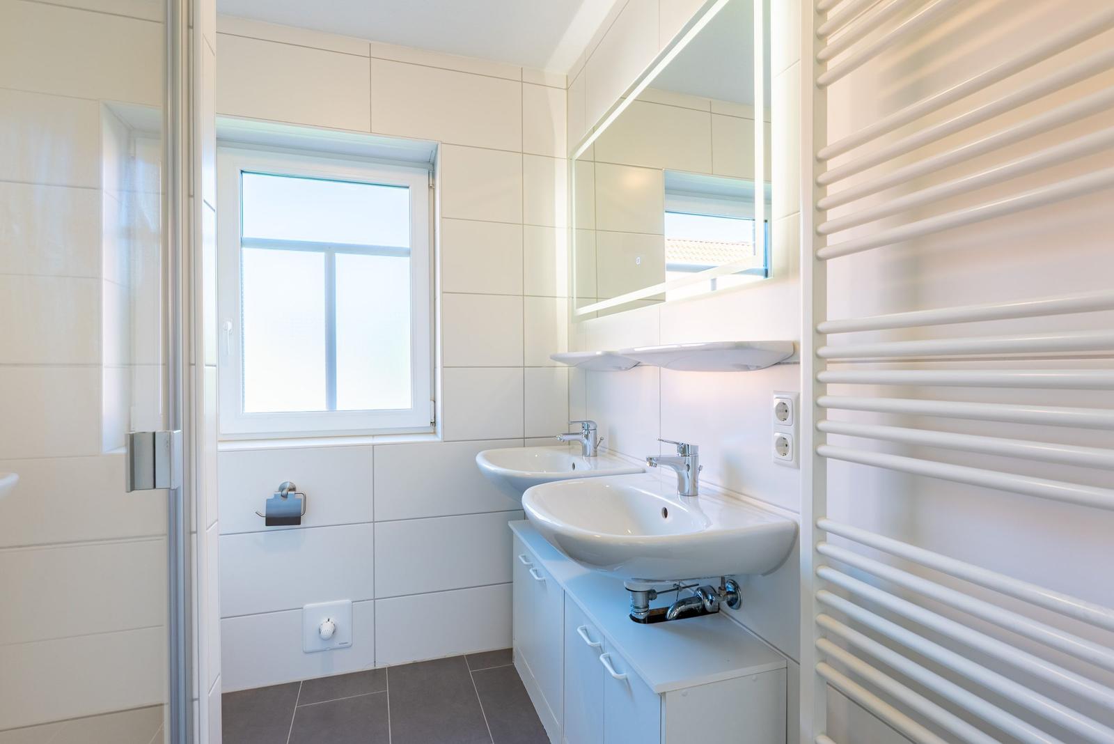Badezimmer mit zwei Waschbecken, Spiegelschrank und Heizkörper.